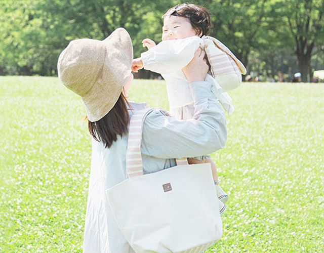 お揃いのリュックとトートを背負って赤ちゃんを抱き上げるママ