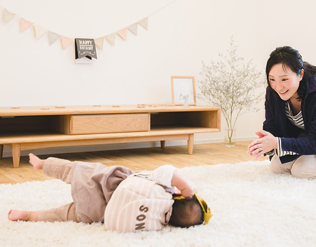 一升餅を背負って転ぶ赤ちゃんと笑顔で見守る母親