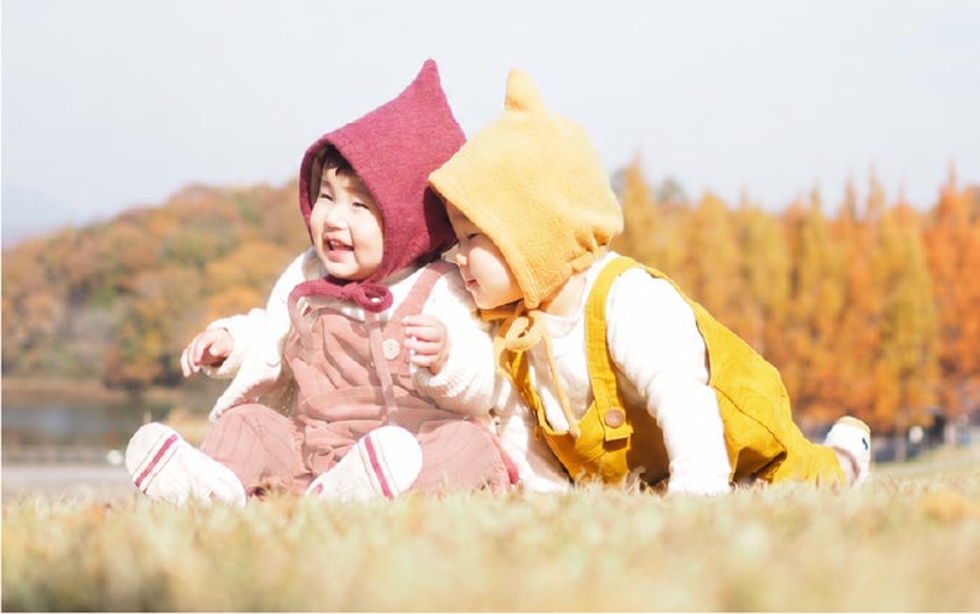こびと帽子とロンパースを着て、秋の芝生に座る赤ちゃんたち