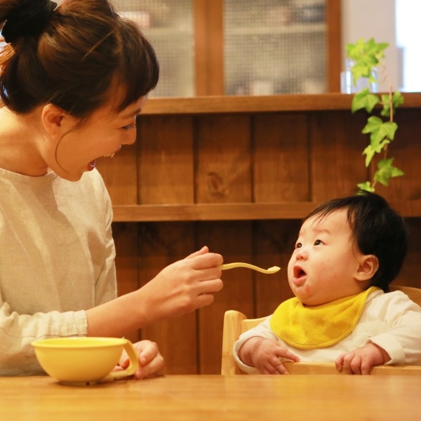 ハイチェアで離乳食を食べる赤ちゃんにスプーンを差し出すママ ― iiwan食器使用例